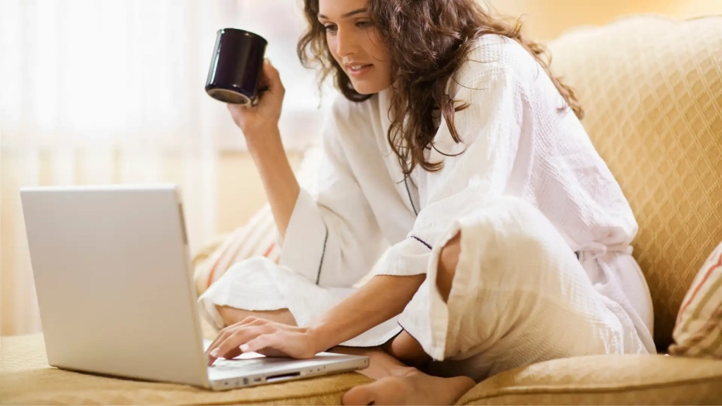 A person holding a cup of coffee while using their laptop